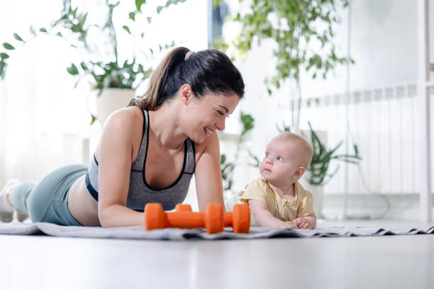 Portrait of a happy mother and her baby lying on their stomachs on the exercise mat and looking at each other. Weights are on the mat too.
